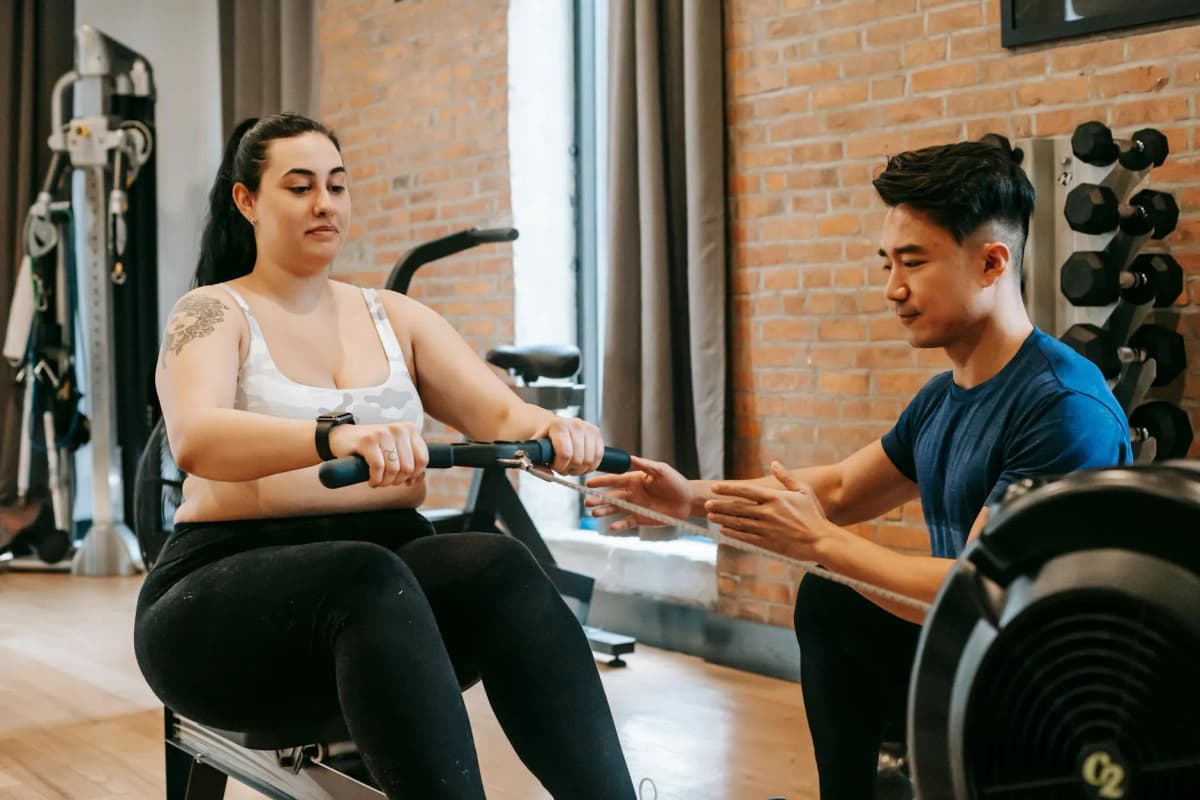 Personal trainer assisting a woman on a rowing machine
